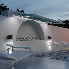 Modern outdoor lounge area at dusk with white lounge chairs by a pool, a curved bench with striped cushions built into a white wall, subtle lighting, and trees in the background.
