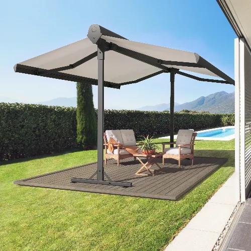 A modern outdoor patio setup with two cushioned chairs and a small table under a large double-sided canopy. The area overlooks a swimming pool, lush green hedge, and mountains in the background on a sunny day.