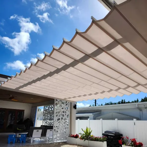 A modern outdoor patio with a retractable cream-colored fabric pergola, white privacy fence, decorative screen, lounge seating, potted plants, and blue sky with clouds overhead.