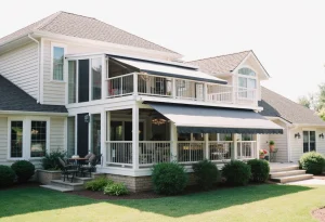 Two-story beige house with white trim and a large porch, featuring two black-and-white striped retractable awnings. The porch overlooks a green lawn with shrubs and patio seating.